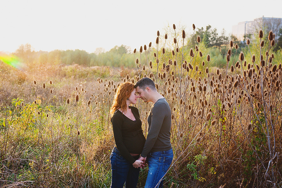 un couple de futurs parents dans un champ et la lumière du soleil couchant